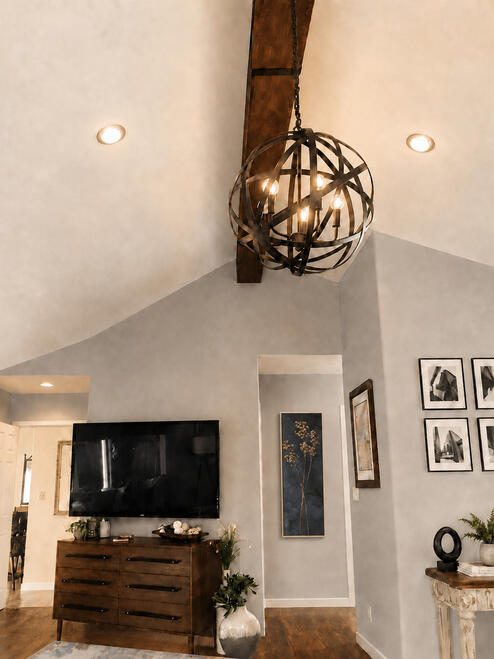 Warm Industrial — Embracing high volume and architectural character. To anchor this room's soaring vaulted ceiling, we highlighted a rustic dark wood ceiling beam with a commanding, spherical iron cage chandelier.